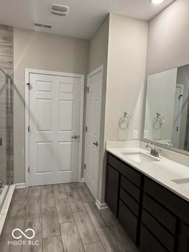 bathroom with wood finish floors, a shower stall, a sink, visible vents, and double vanity