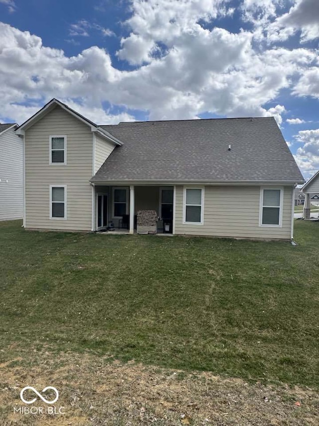 rear view of property featuring a patio, a shingled roof, and a lawn