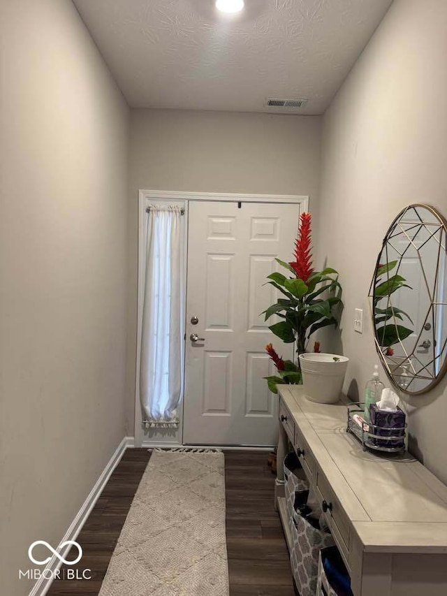 foyer entrance featuring dark wood-type flooring, baseboards, a textured ceiling, and visible vents