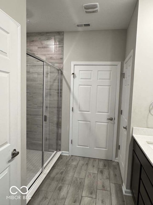 full bath with wood tiled floor, vanity, a shower stall, and visible vents