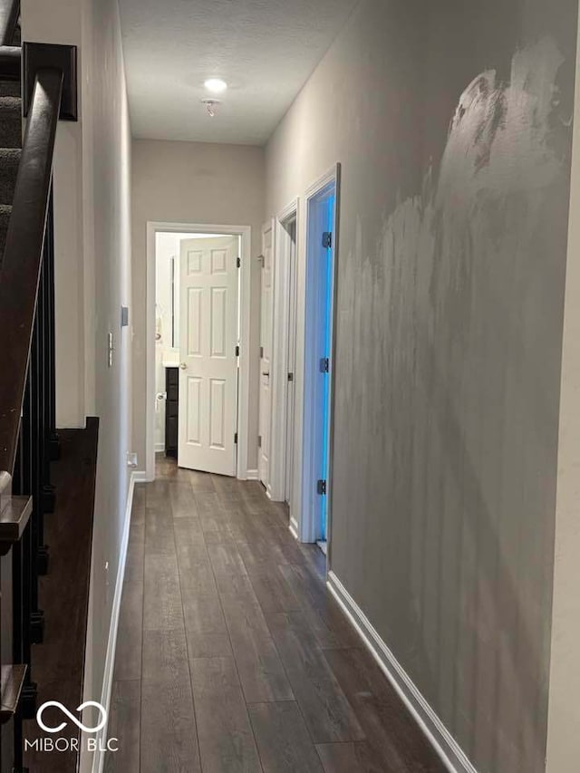 hallway with dark wood-type flooring, baseboards, and stairway