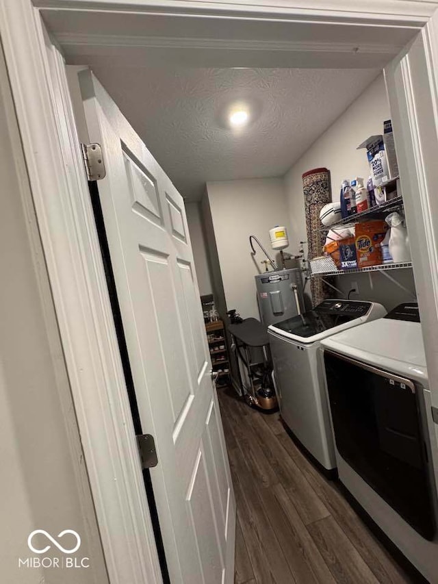 laundry area with water heater, washing machine and clothes dryer, a textured ceiling, dark wood finished floors, and laundry area