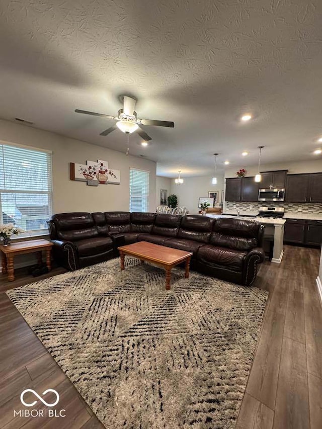 living room with visible vents, ceiling fan, dark wood-type flooring, and a textured ceiling