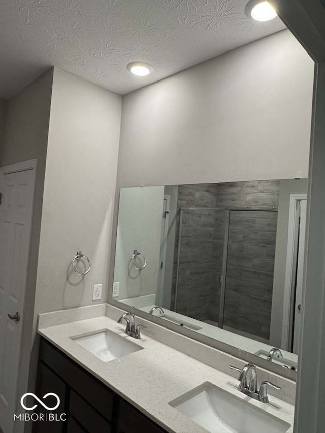 bathroom with double vanity, a sink, a tile shower, and a textured ceiling