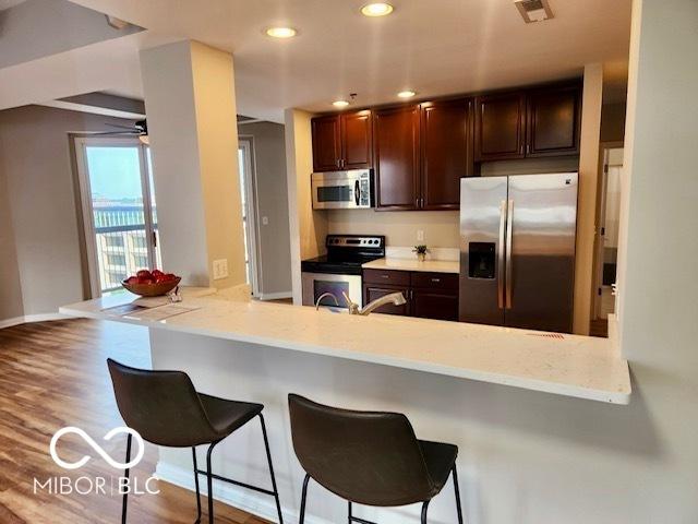 110 E Washington St Unit 802, Indianapolis, IN 46204 - kitchen with appliances with stainless steel finishes, a kitchen bar, light countertops, dark brown cabinets, and recessed lighting