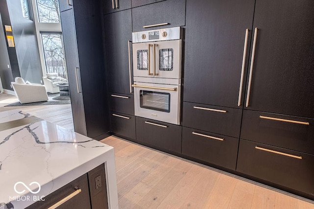 395 Breakwater Dr, Fishers, IN 46037 - kitchen with light stone countertops, light wood-style flooring, dark cabinets, and stainless steel double oven