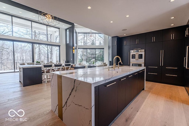 395 Breakwater Dr, Fishers, IN 46037 - kitchen with a large island with sink, light wood-type flooring, double oven, a sink, and modern cabinets