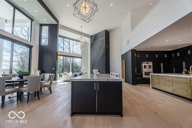 395 Breakwater Dr, Fishers, IN 46037 - kitchen with light wood-style flooring, stainless steel double oven, a spacious island, dark cabinetry, and a notable chandelier