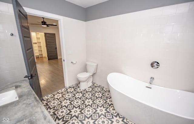 bathroom with toilet, a freestanding tub, wood finished floors, a ceiling fan, and a sink