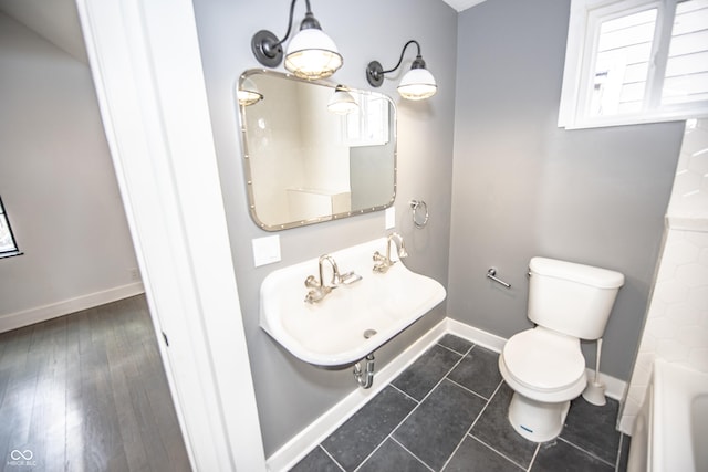 bathroom with tile patterned flooring, a tub, toilet, baseboards, and a sink