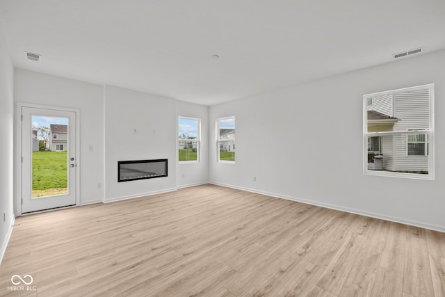 unfurnished living room with plenty of natural light, light wood-style floors, baseboards, and a glass covered fireplace