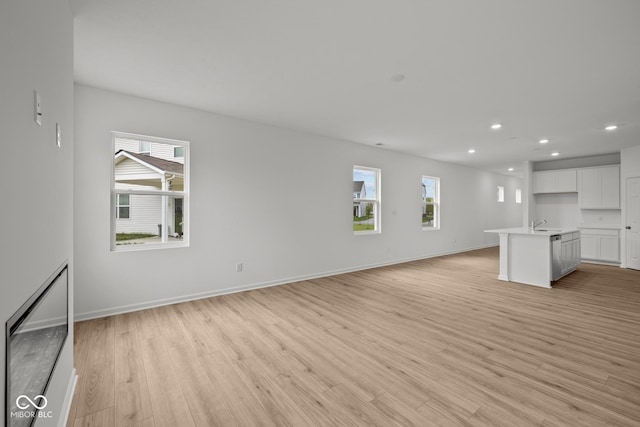 unfurnished living room featuring light wood finished floors, recessed lighting, baseboards, and a sink