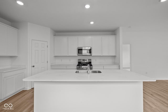 kitchen featuring appliances with stainless steel finishes, light wood-style flooring, white cabinets, a center island with sink, and recessed lighting