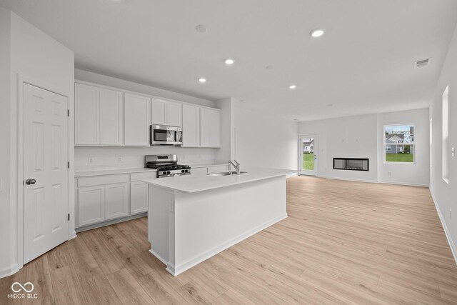 kitchen featuring stainless steel appliances, white cabinets, light wood-style flooring, a sink, and recessed lighting