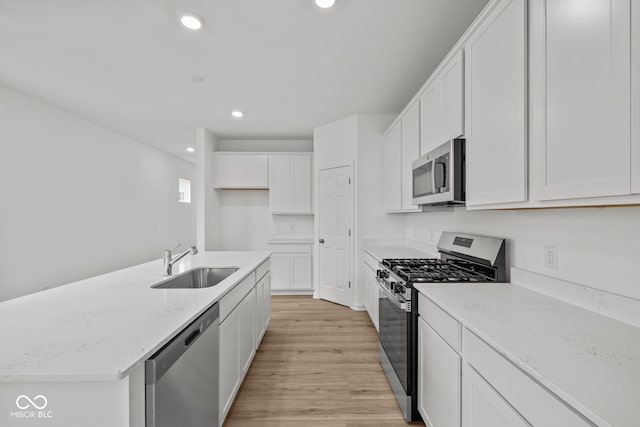 kitchen featuring appliances with stainless steel finishes, a sink, light wood finished floors, white cabinetry, and recessed lighting