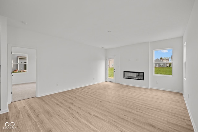 unfurnished living room featuring light wood-style flooring, baseboards, and a glass covered fireplace