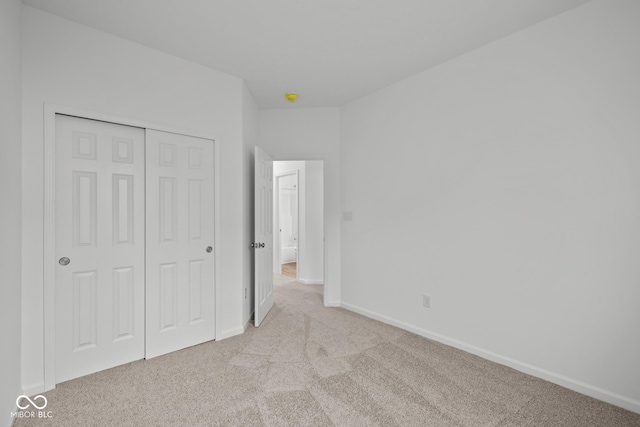 unfurnished bedroom featuring light colored carpet, a closet, and baseboards