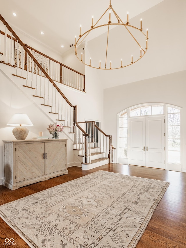 foyer entrance with stairway, wood finished floors, a chandelier, a high ceiling, and recessed lighting