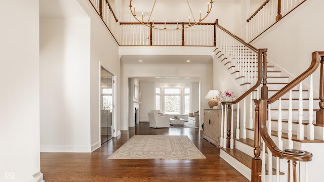 foyer entrance featuring a towering ceiling, stairway, wood finished floors, a chandelier, and baseboards