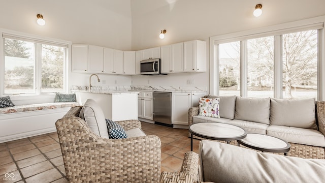 kitchen featuring stainless steel appliances, high vaulted ceiling, open floor plan, white cabinets, and light stone countertops