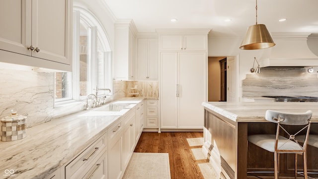 kitchen with a sink, light wood-style flooring, decorative backsplash, custom range hood, and light stone counters