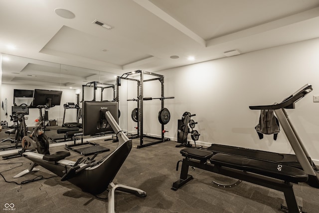 exercise room featuring a raised ceiling, carpet flooring, and baseboards