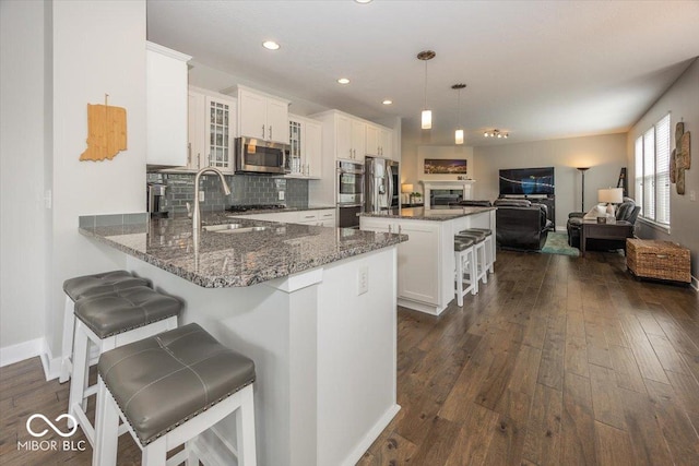kitchen with appliances with stainless steel finishes, a sink, glass insert cabinets, tasteful backsplash, and dark stone counters