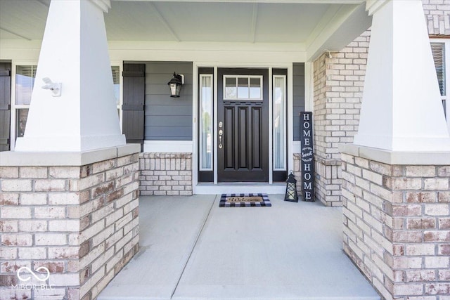 doorway to property featuring a porch and brick siding
