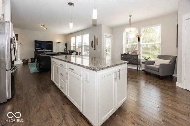kitchen with open floor plan, freestanding refrigerator, white cabinetry, light stone countertops, and dark wood finished floors