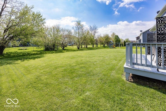 view of grassy yard featuring a playground and a wooden deck