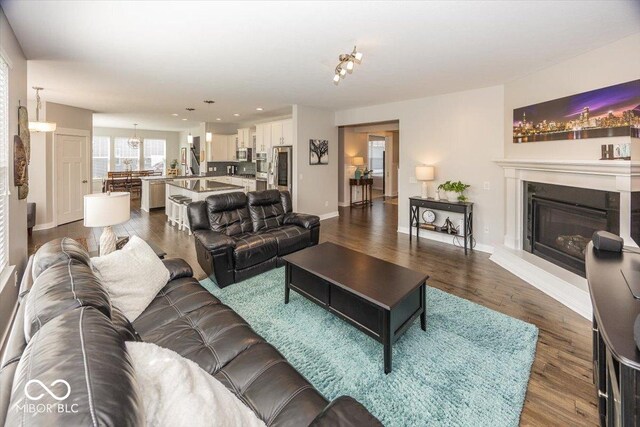 living area with a glass covered fireplace, recessed lighting, dark wood finished floors, baseboards, and a chandelier