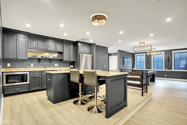 5120 Melbourne Pl, Zionsville, IN 46077 - kitchen featuring stainless steel appliances, light wood-style flooring, a center island, tasteful backsplash, and a kitchen bar