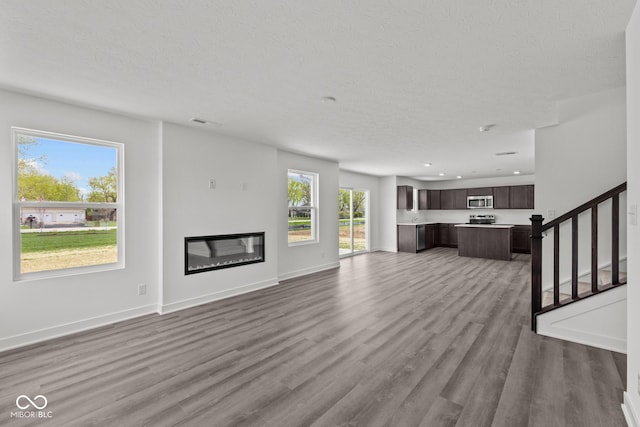 3913 Highcrest Rd, Indianapolis, IN 46239 - unfurnished living room featuring wood finished floors, a glass covered fireplace, a textured ceiling, stairway, and baseboards