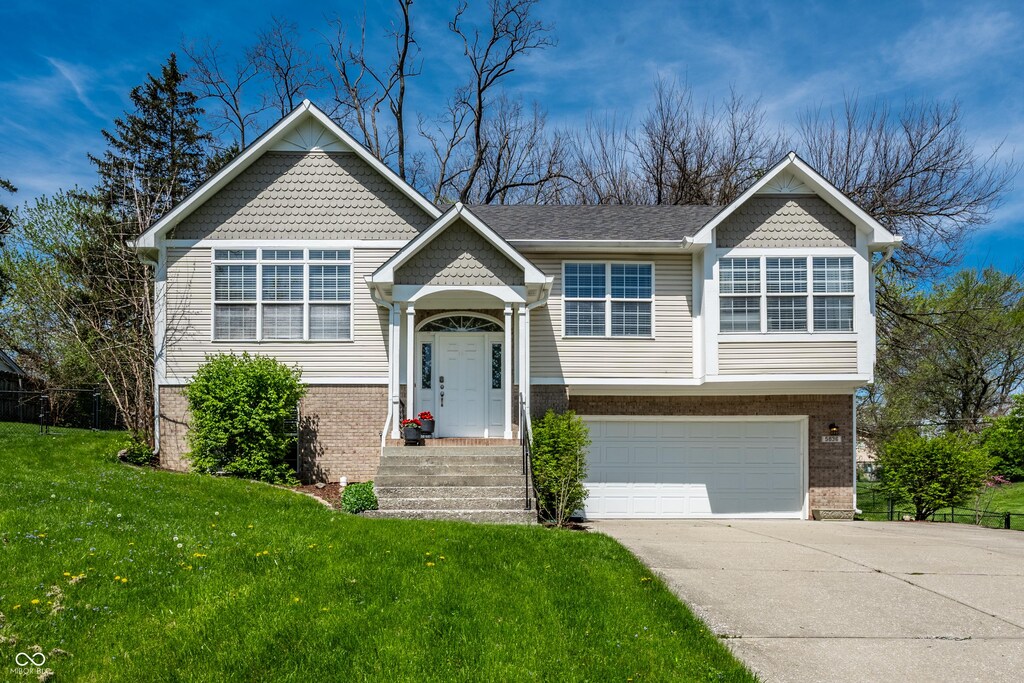 split foyer home featuring brick siding, an attached garage, driveway, and a front lawn