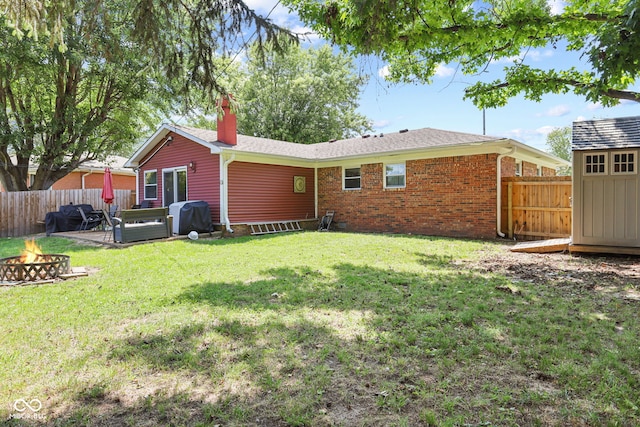 rear view of property with a lawn, an outdoor fire pit, a fenced backyard, and an outdoor structure