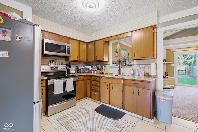kitchen featuring light carpet, appliances with stainless steel finishes, brown cabinetry, a textured ceiling, and a sink