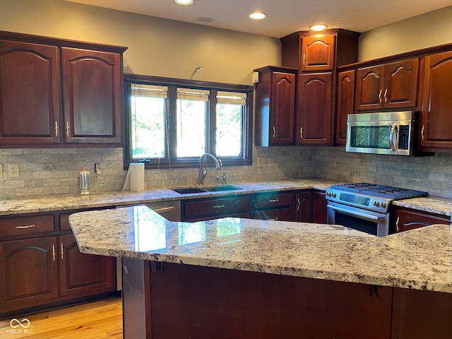11967 Windpointe Pass, Carmel, IN 46033 - kitchen with stainless steel appliances, a sink, light stone counters, light wood-style flooring, and backsplash