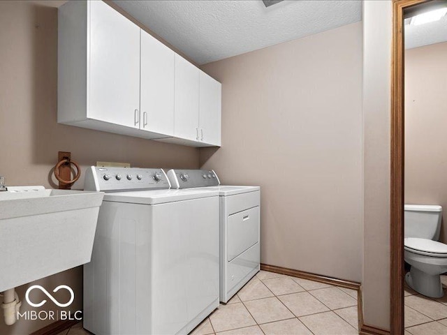 laundry room with light tile patterned flooring, a textured ceiling, a sink, cabinet space, and independent washer and dryer