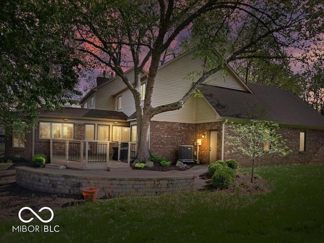 back of property at dusk featuring a lawn, brick siding, and central AC unit