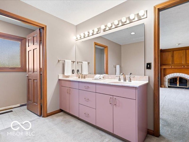 full bath featuring double vanity, a textured ceiling, visible vents, a sink, and baseboards