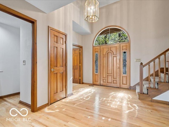 entrance foyer featuring a high ceiling, a notable chandelier, baseboards, wood finished floors, and stairway