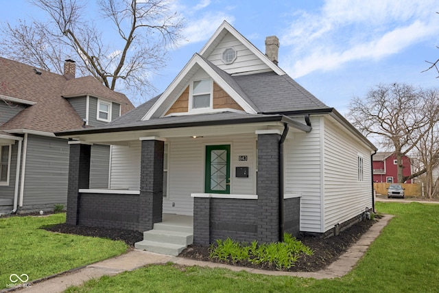 843 N Oxford St, Indianapolis, IN 46201 - view of front facade with a porch, a chimney, a front lawn, brick siding, and roof with shingles