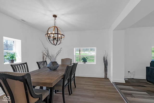 dining area featuring a notable chandelier, baseboards, visible vents, and wood finished floors