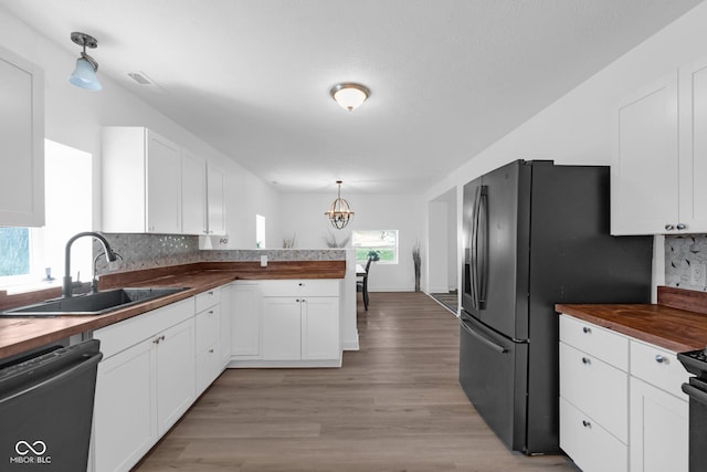 kitchen featuring butcher block counters, dishwashing machine, a sink, and black fridge