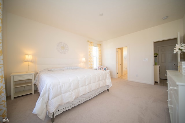 bedroom with baseboards, light carpet, and ensuite bath