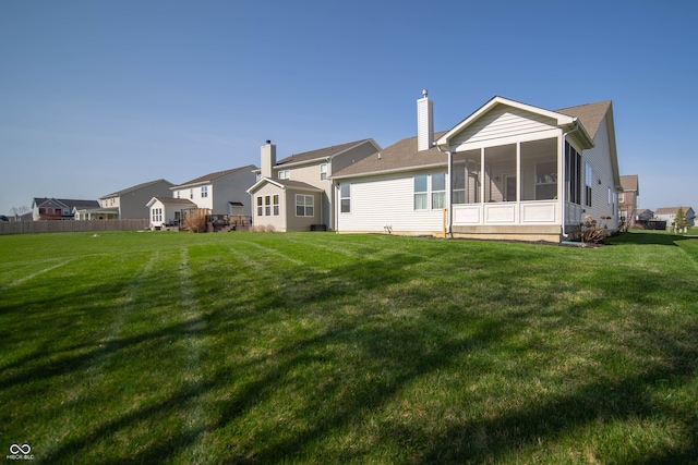 back of house featuring a lawn, a chimney, and a sunroom
