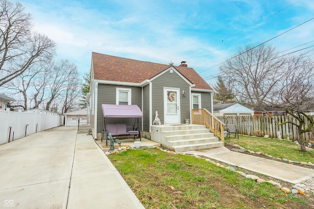 bungalow featuring fence, a chimney, roof with shingles, and a front lawn