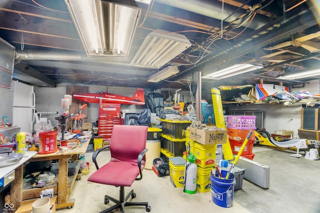 unfinished basement with a workshop area and freestanding refrigerator