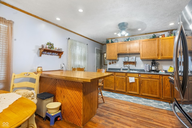 kitchen featuring a sink, brown cabinetry, wooden counters, wood finished floors, and ornamental molding