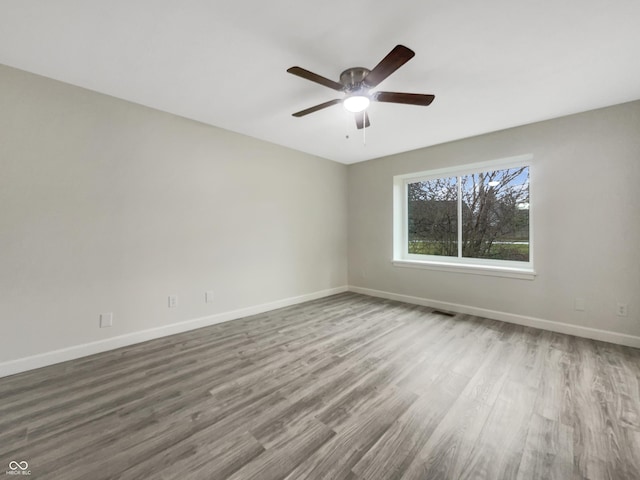 spare room featuring a ceiling fan, visible vents, baseboards, and wood finished floors